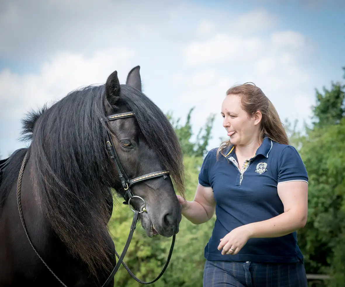 A woman gently pets a brown horse, smiling as she interacts with the animal in a serene outdoor setting.