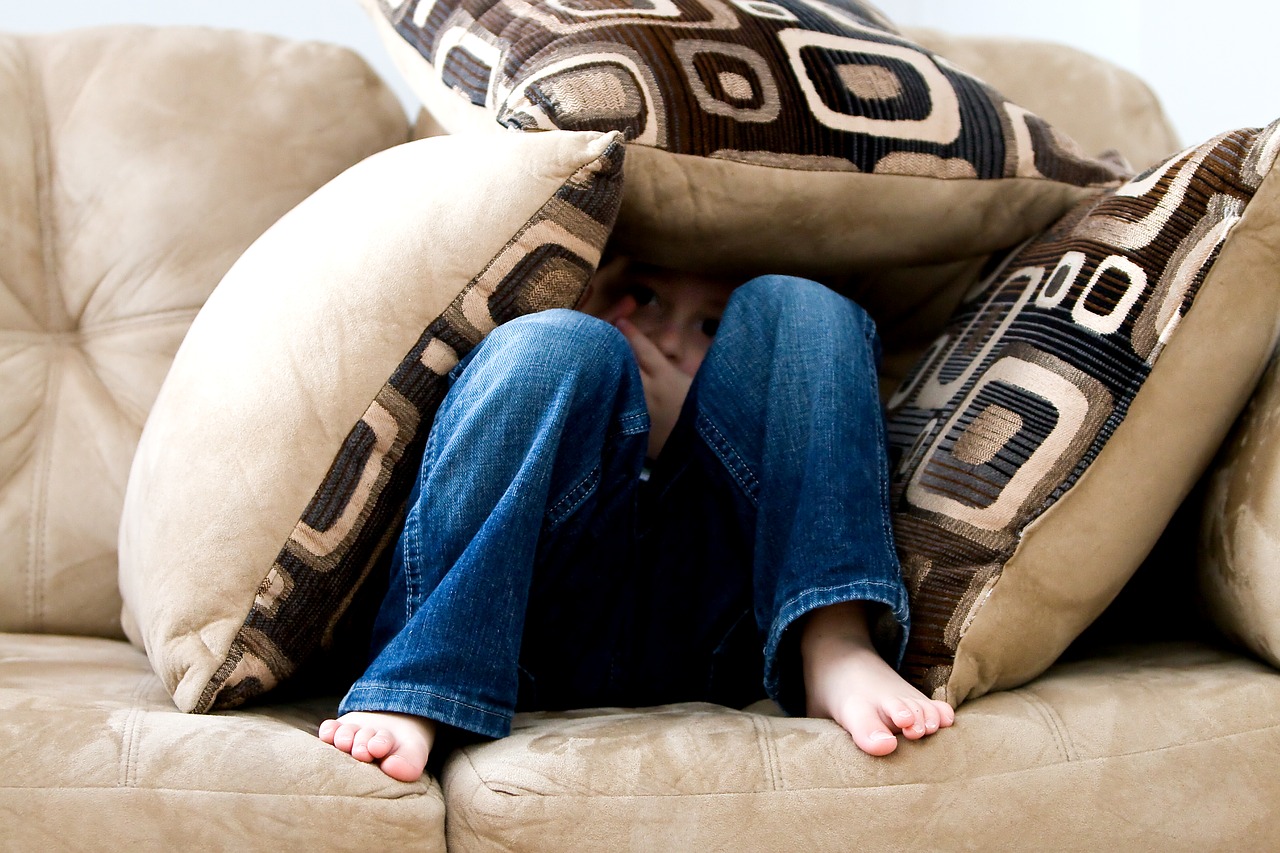 image of a boy hiding behind cushions on a sofa in fear